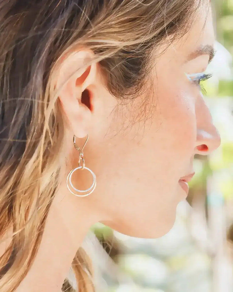 Close-up of a woman wearing a gold hoop earring with a blurred natural background