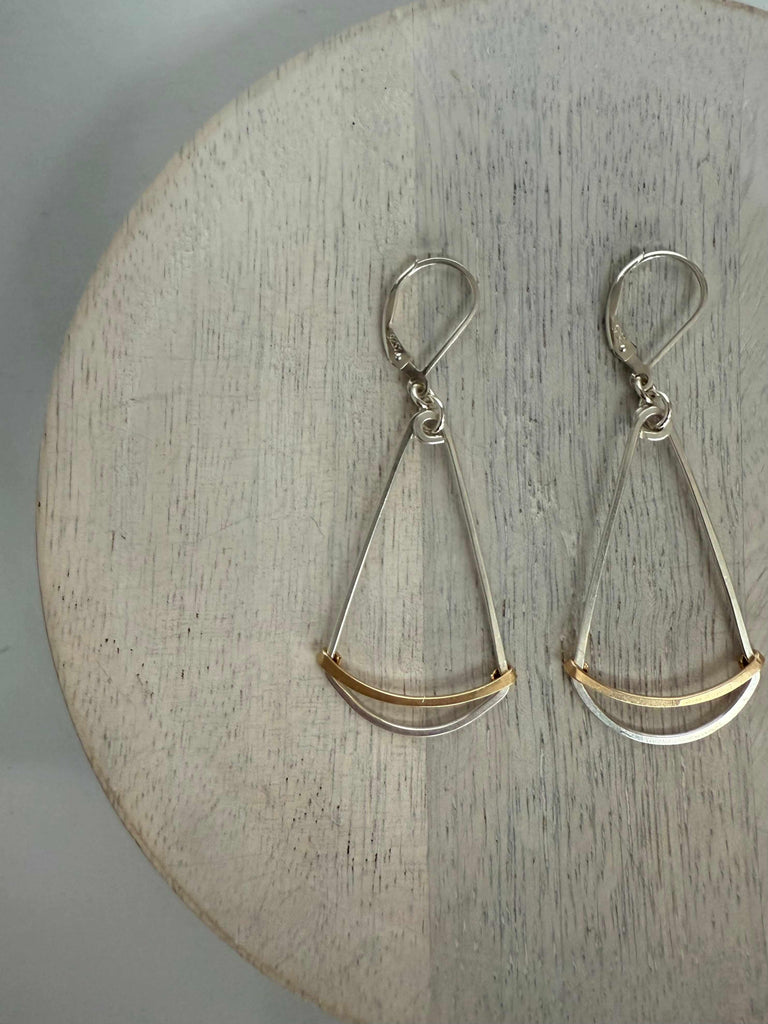 Pair of silver dangle earrings with gold accents on a wooden surface
