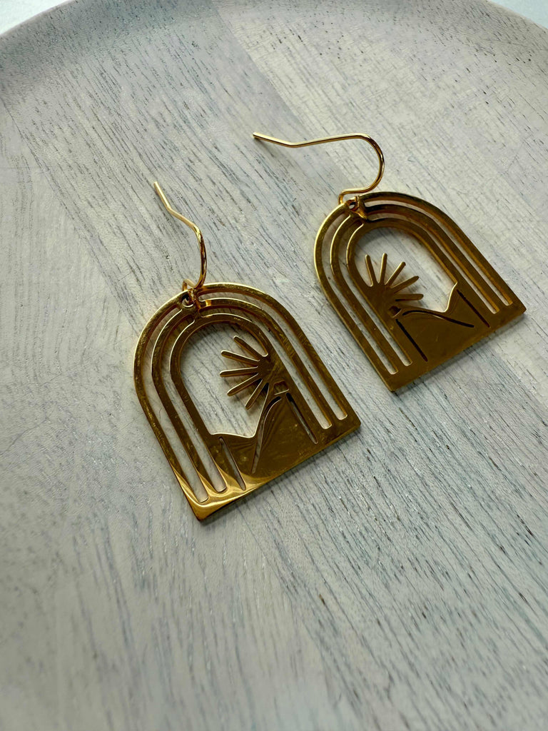 Gold arch-shaped sunrise earrings on a light wooden surface