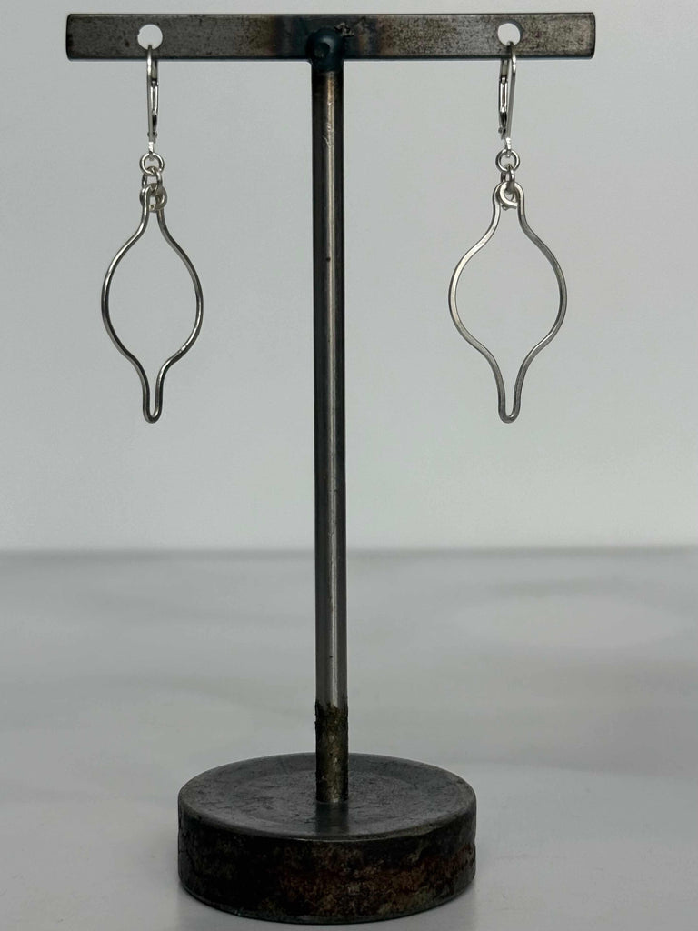 Pair of silver ogee shaped earrings on a black stand against a gray background