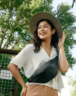 Woman wearing a wide-brimmed hat and white shirt with a black waist bag outdoors.