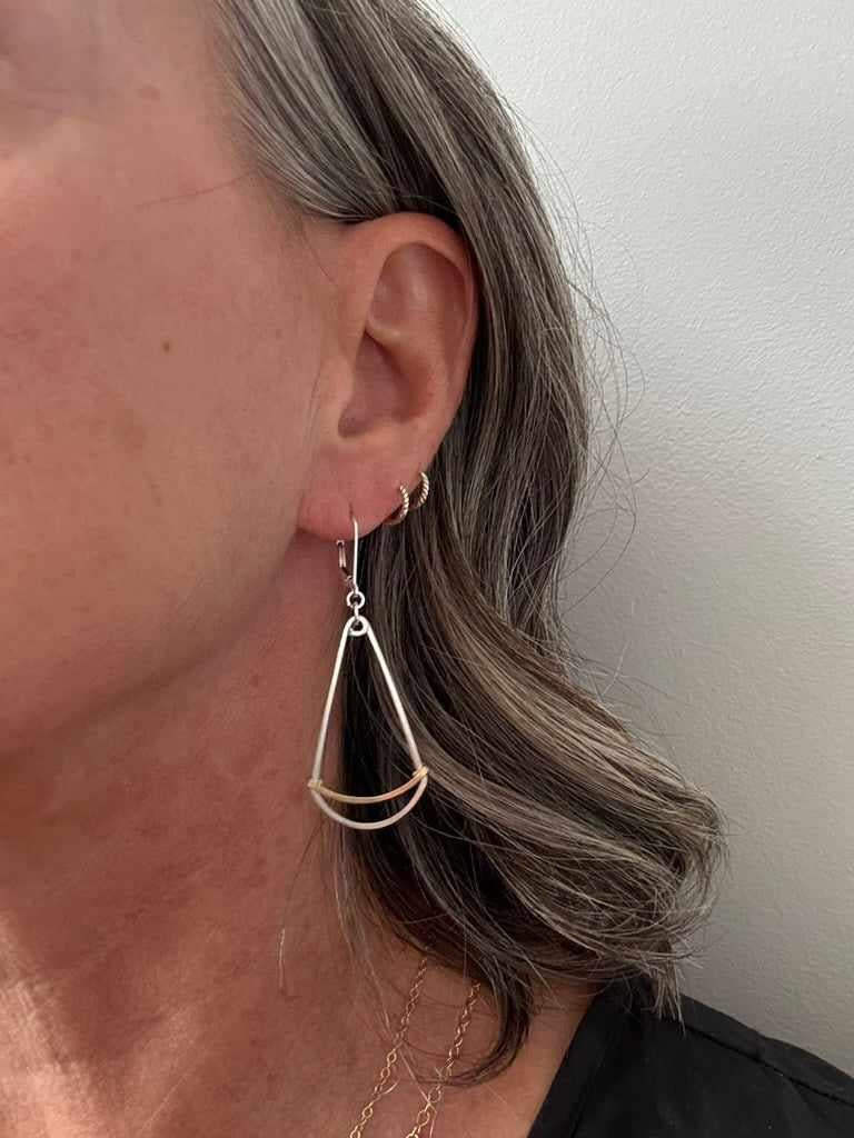 Close-up of a person wearing a gold and silver mixed metal earring against a neutral background