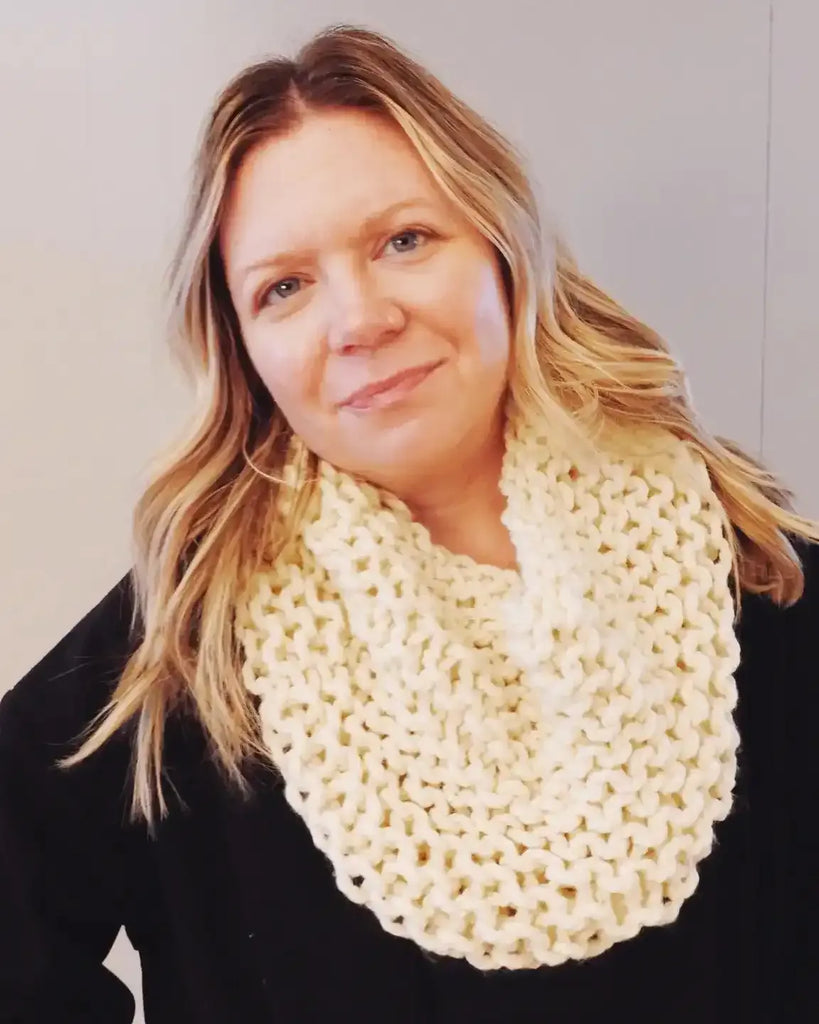 Woman wearing a cream-colored knitted scarf against a plain background