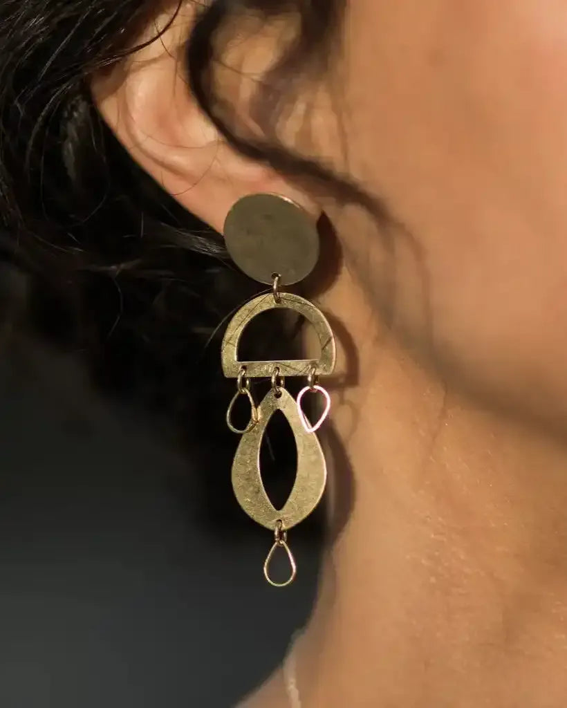 Close-up of a person wearing geometric brass chandelier earrings 