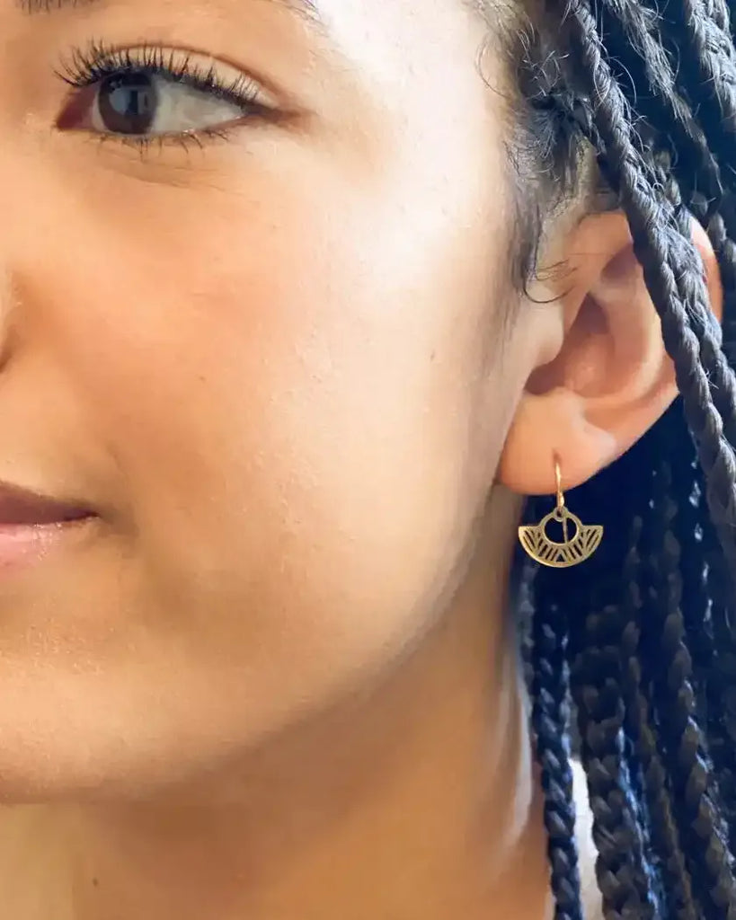 Close-up of a woman wearing a gold earring with braided hair.