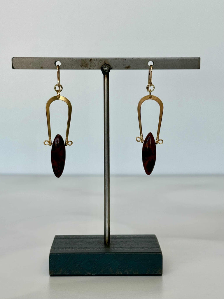 Pair of earrings with gold hooks and maroon stones on a black stand against a light gray background