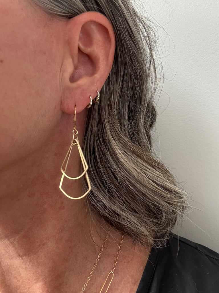 Close-up of an ear wearing gold double fan shaped earrings with a plain background