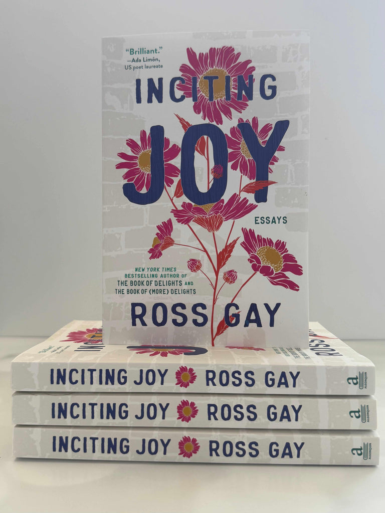 Stack of books titled 'Inciting Joy' by Ross Gay on a white surface with a gray background.