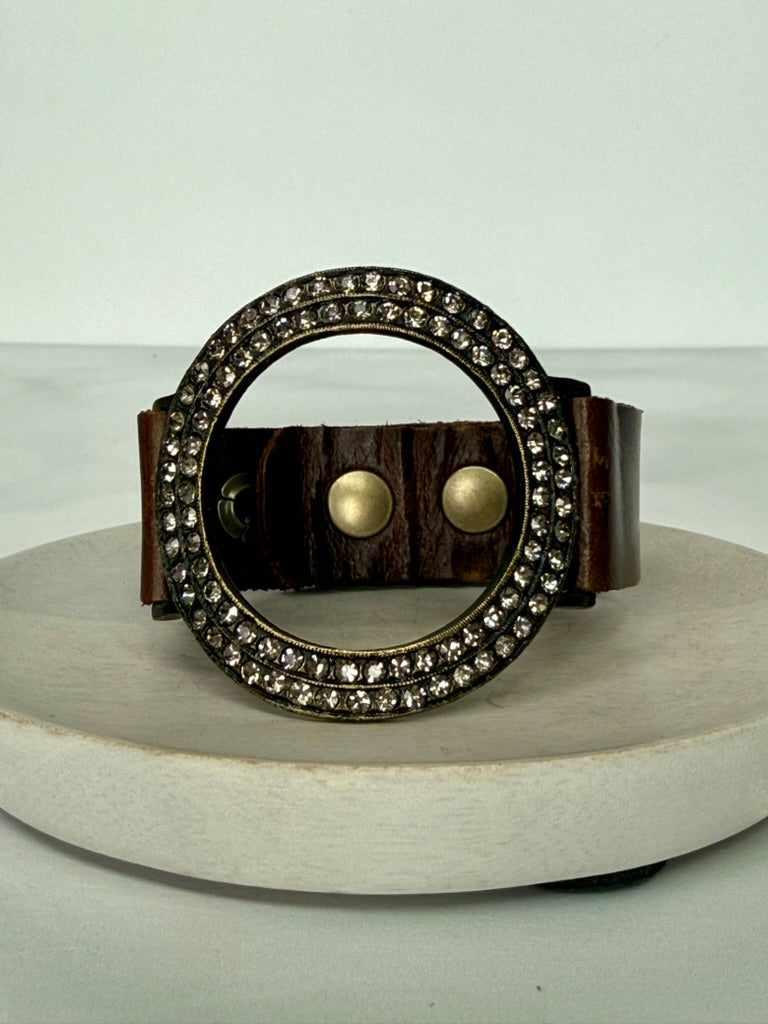 Brown leather bracelet with circular metal design and embedded stones on a white background