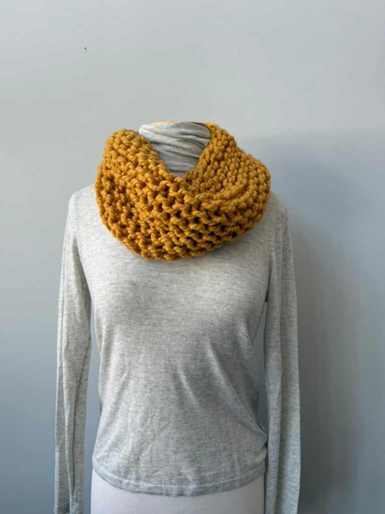 Mustard yellow knitted circle scarf on a mannequin against a plain background