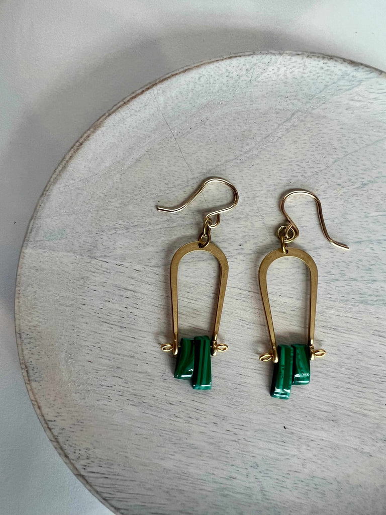 A pair of vintage brass earrings with green malachite beads and gold-filled ear wires, displayed on a wooden surface.