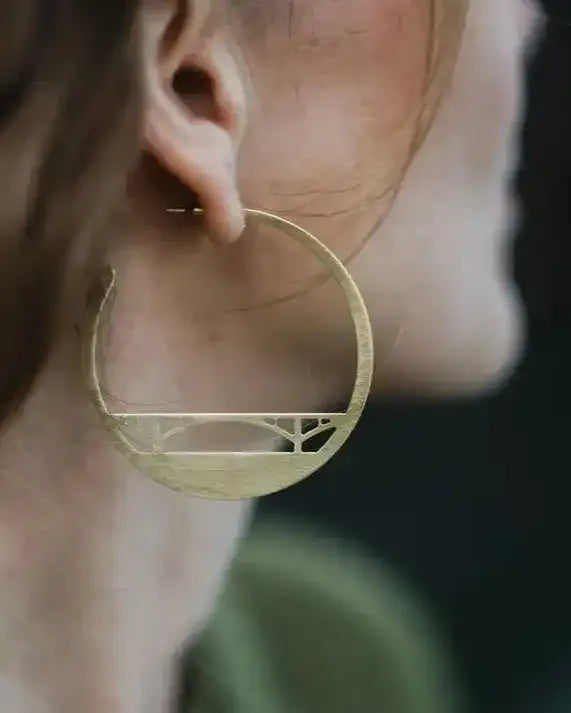 Brass Bridge  hoop earring worn by a person with a blurred background