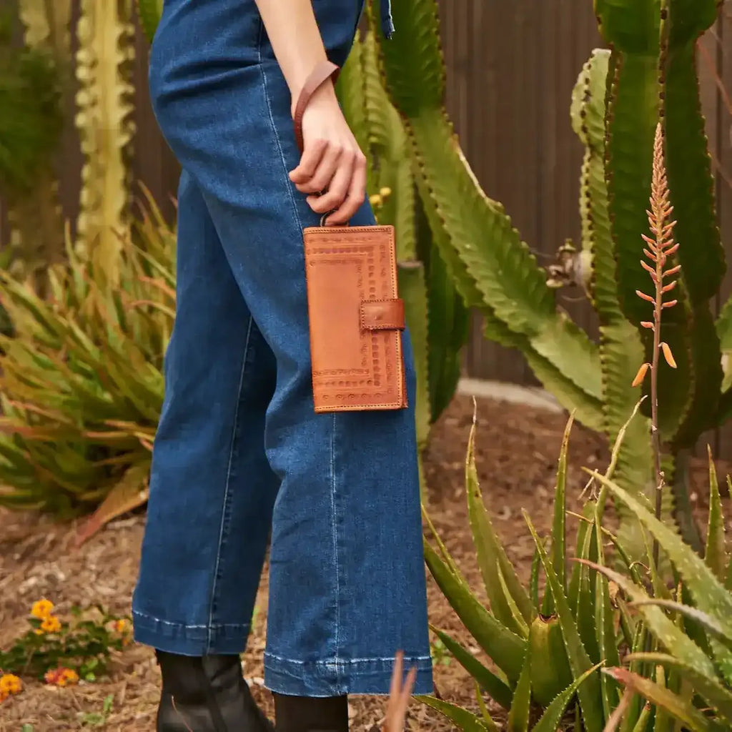 Person holding a brown leather wallet with plants in the background