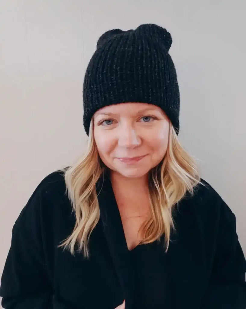 Person wearing a black knit beanie with bear ears against a plain background