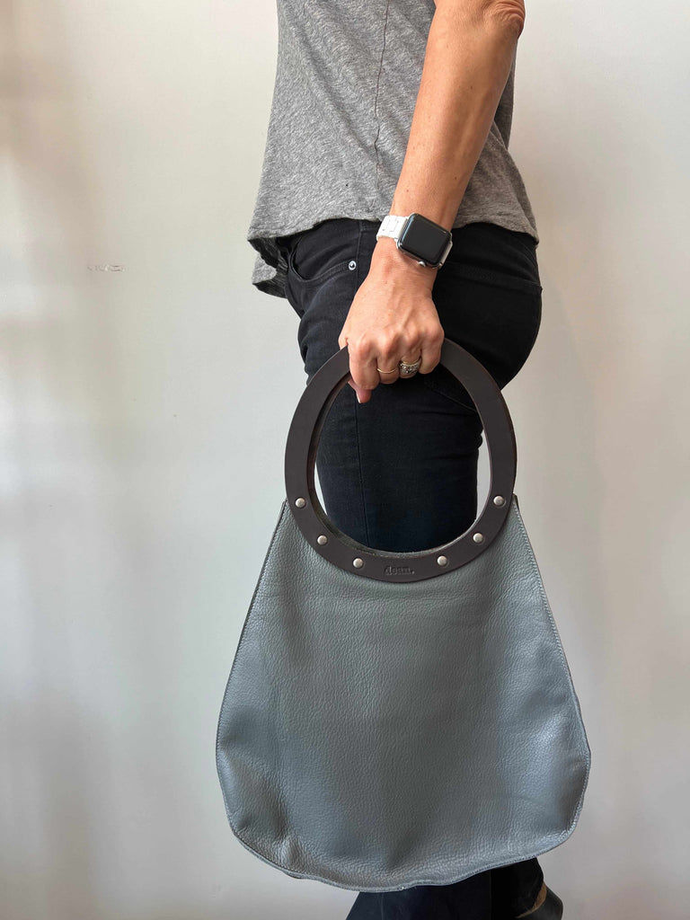 Woman holding grey and brown teardrop shaped bag with latigo leather handle